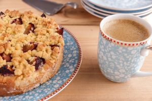 A round coffee cake with crumble top on a blue dish with a cup of coffee