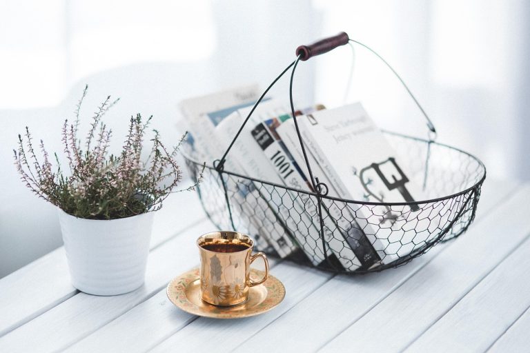 a basket of books, plant, and gold coffee cup on a white table