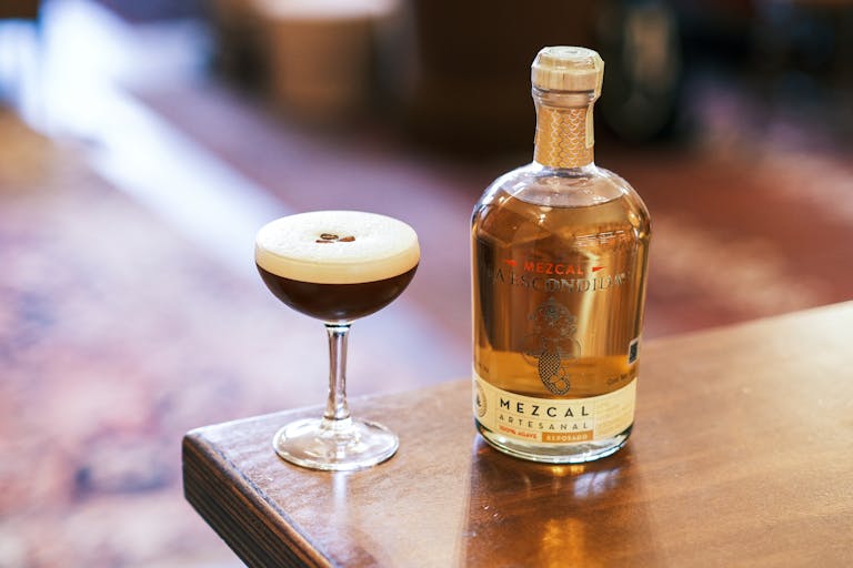 A chic cocktail and mezcal bottle elegantly placed on a wooden table, perfect for upscale settings.