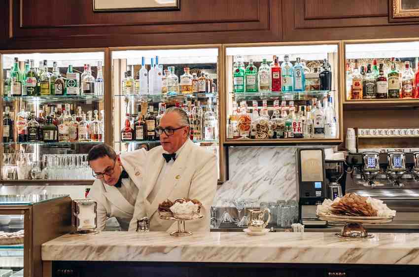 Man in white jacket and black bow tie servicing at the counter of a cafe in Milan Italy